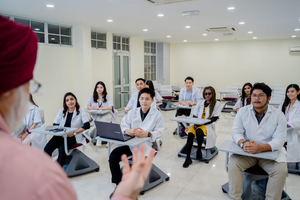 Diverse group of medical students attentively listening to a lecturer in a well-lit, modern classroom setting.