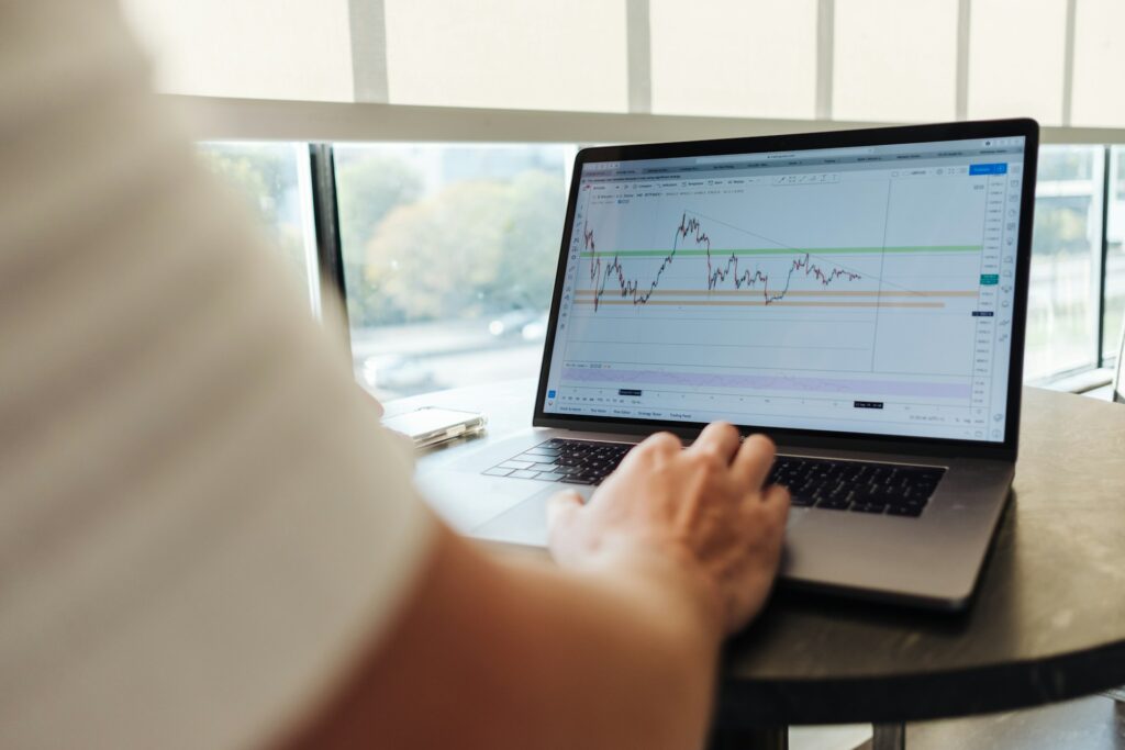 A person analysing financial data on a laptop with graphs displayed on the screen, in a bright office setting.